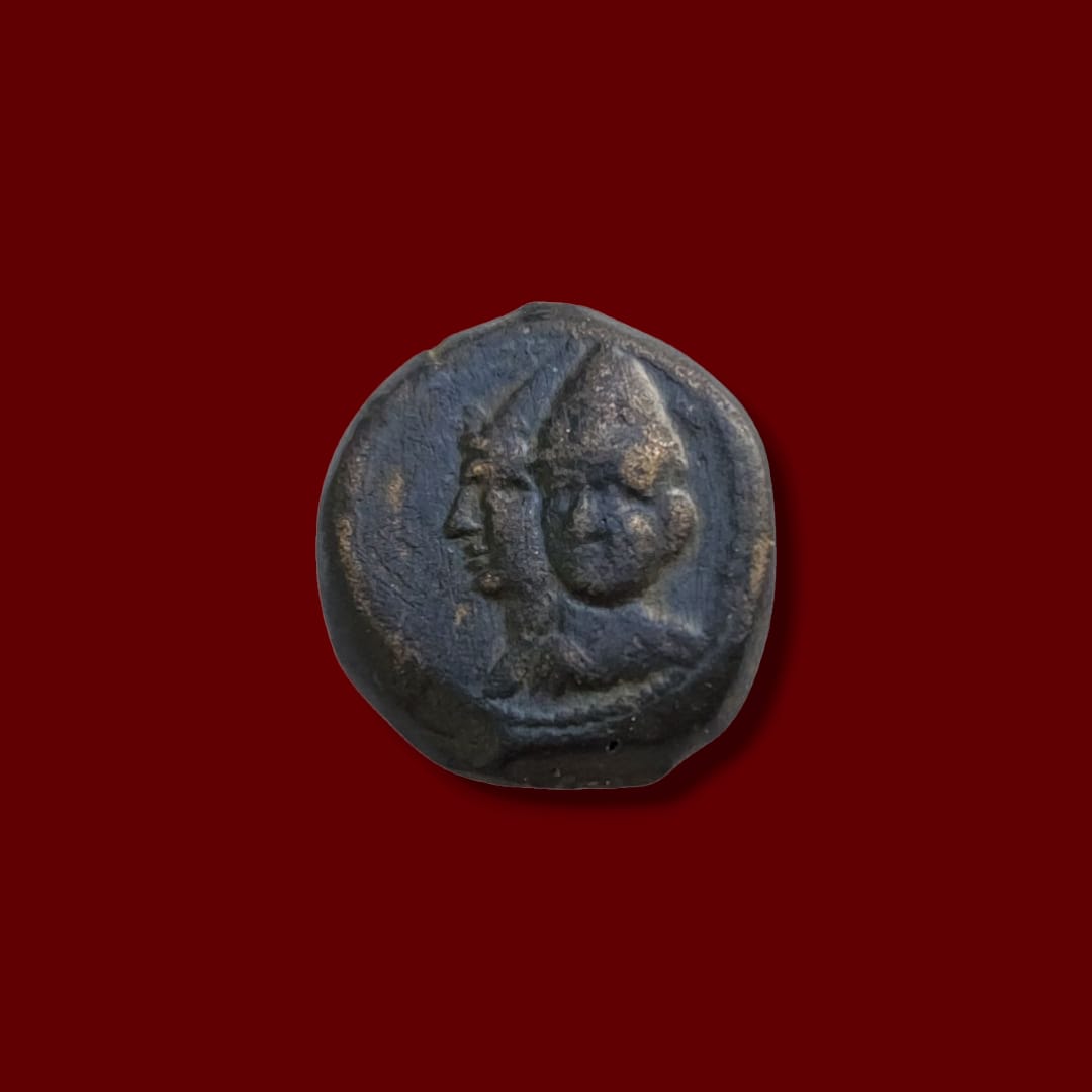 Jugate busts (side-by-side heads) of Seleucid rulers wearing helmets. Ancient Seleucid bronze coin obverse.